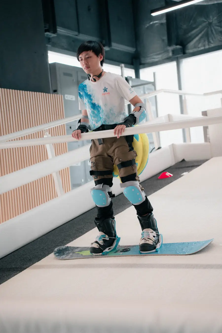 Học viên tập snowboard trên dốc mô phỏng trong nhà, đủ đồ bảo hộ